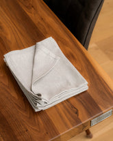 A folded Light Grey cotton napkin on a wooden dining table.