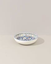 A ceramic hand painted decorative plate with a geometric pattern, predominantly white with blue and gold accents.
