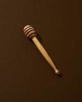 A natural olive wood honey spoon with a solid pattern, lying on a brown surface.