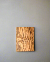 A natural olive wood chopping board displayed on a gray background, highlighting its organic shape, rich wood grain, and smooth, handcrafted finish.
