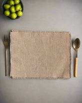 A beige burlap placemat on a gray surface with a fork on the left side and a spoon on the right side, both with wooden handles.