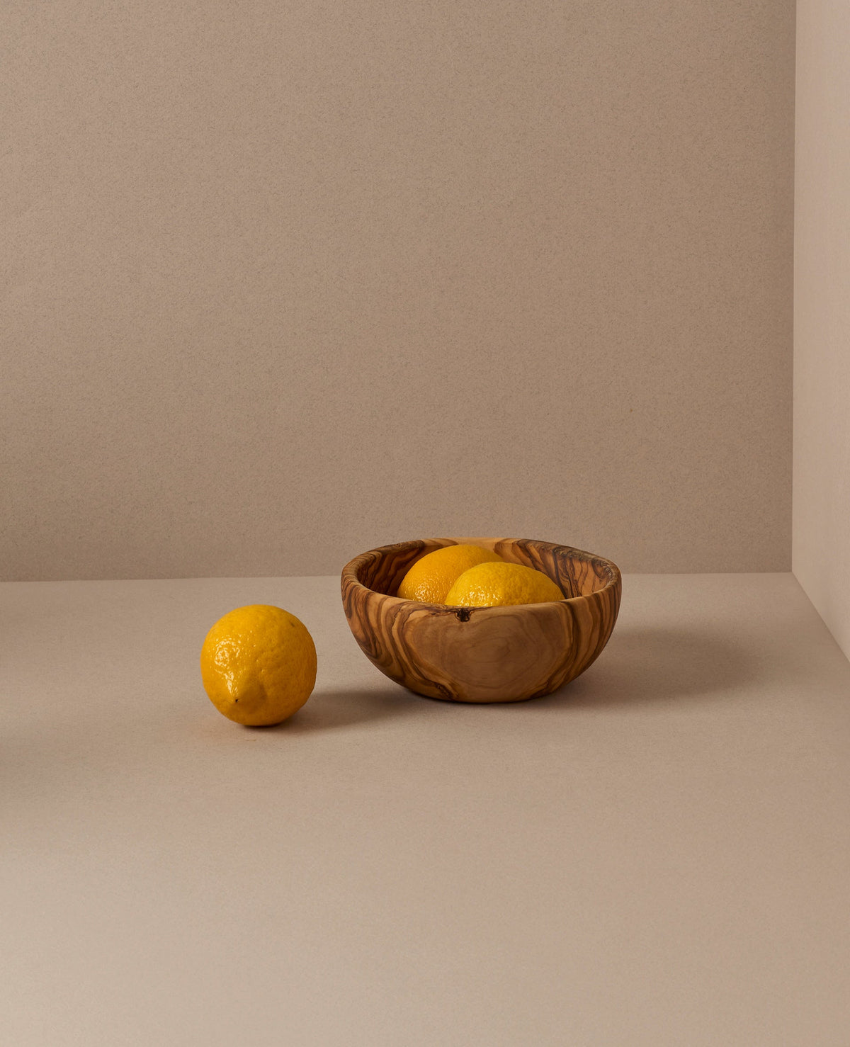 A set of natural olive wood bowls in various sizes, with the smallest bowls containing lemons. The bowls display a beautiful wood grain pattern.