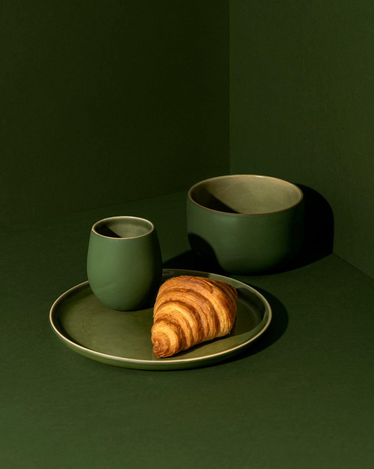 A minimalist white dinnerware set displayed against a neutral background, including a flat salad plate with a dessert, a dinner bowl, and a cup.