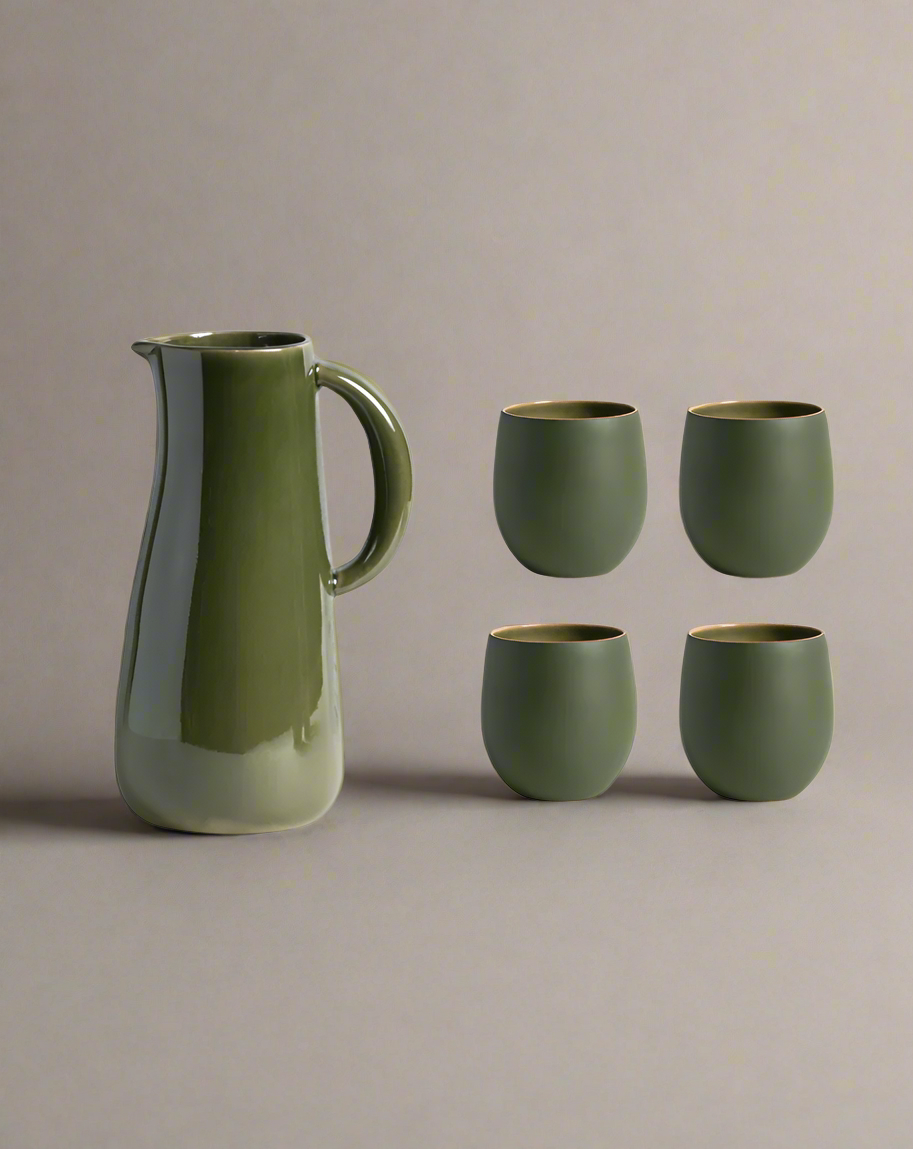 A stoneware jug in green color accompanied by four matching cups, displayed against a neutral background.